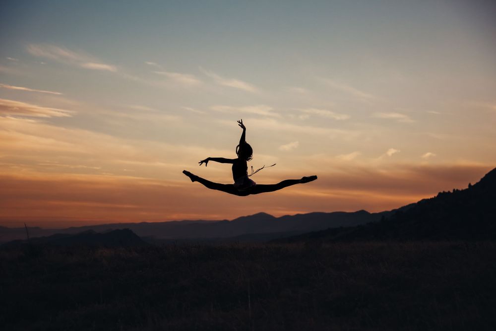 A ballerina leaps in the air silhouetted against a colorful Colorado sunset