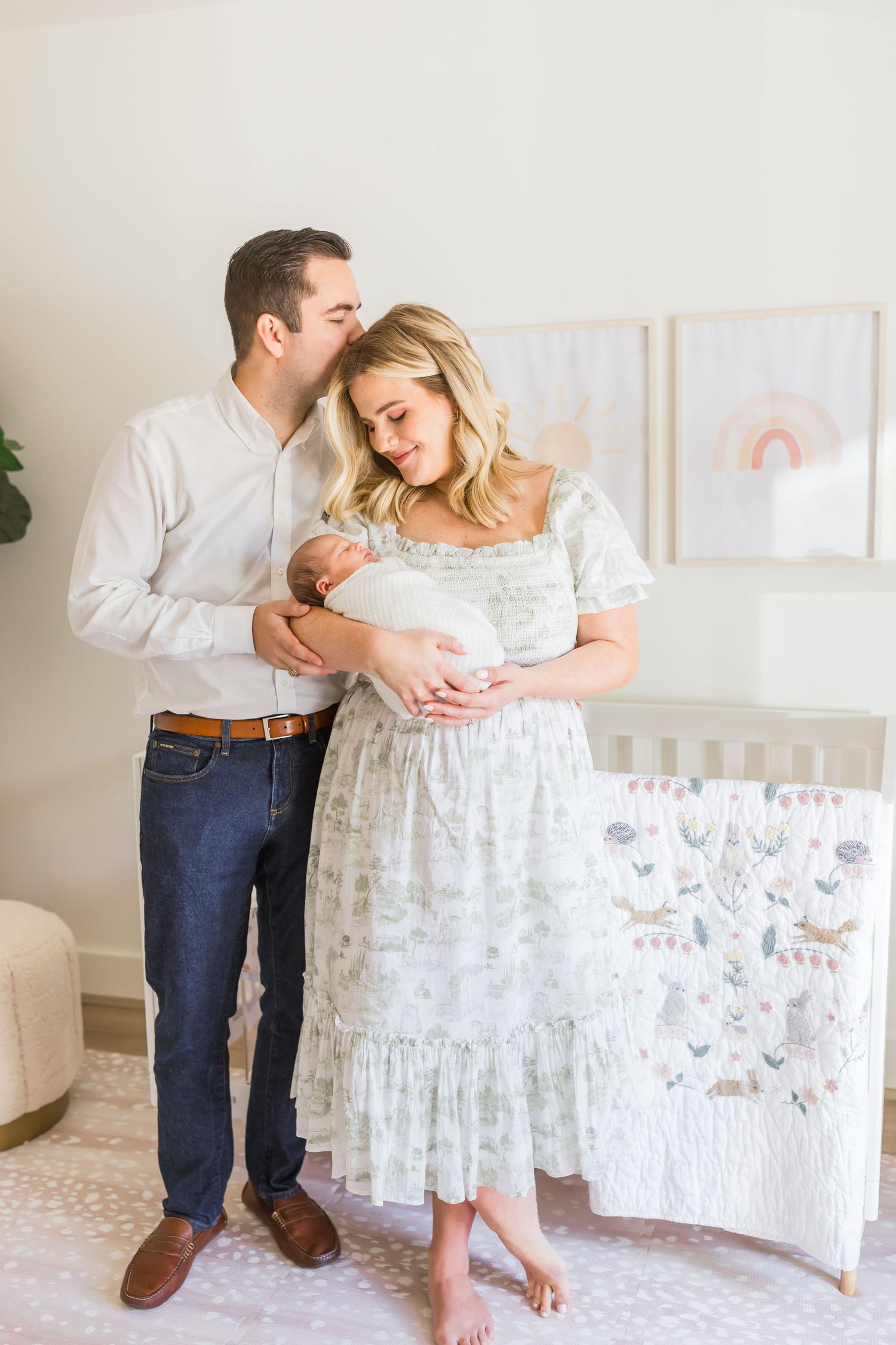 A sweet family moment captured in front of a white crib with pastel rainbow artwork.