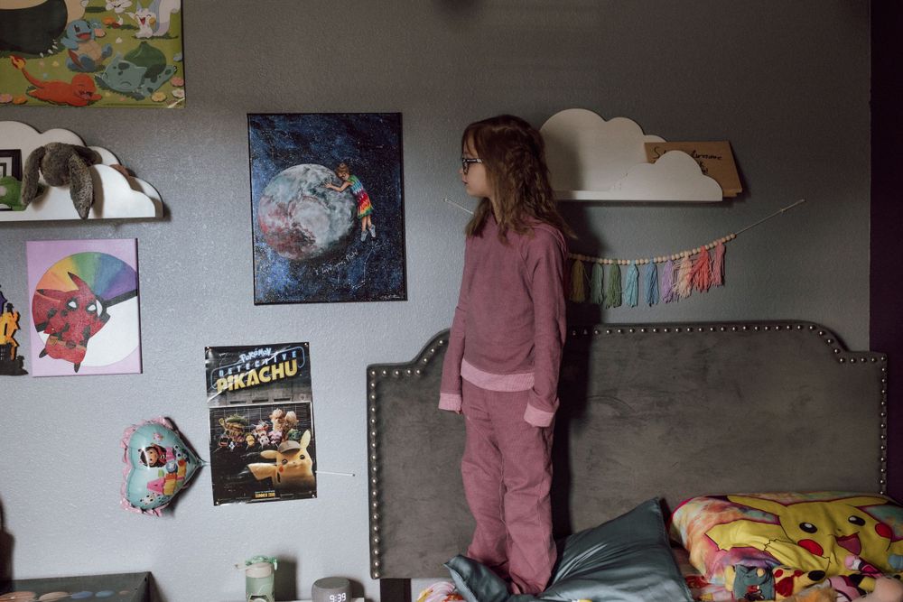 girl standing on her bed pointing at a painting of pluto