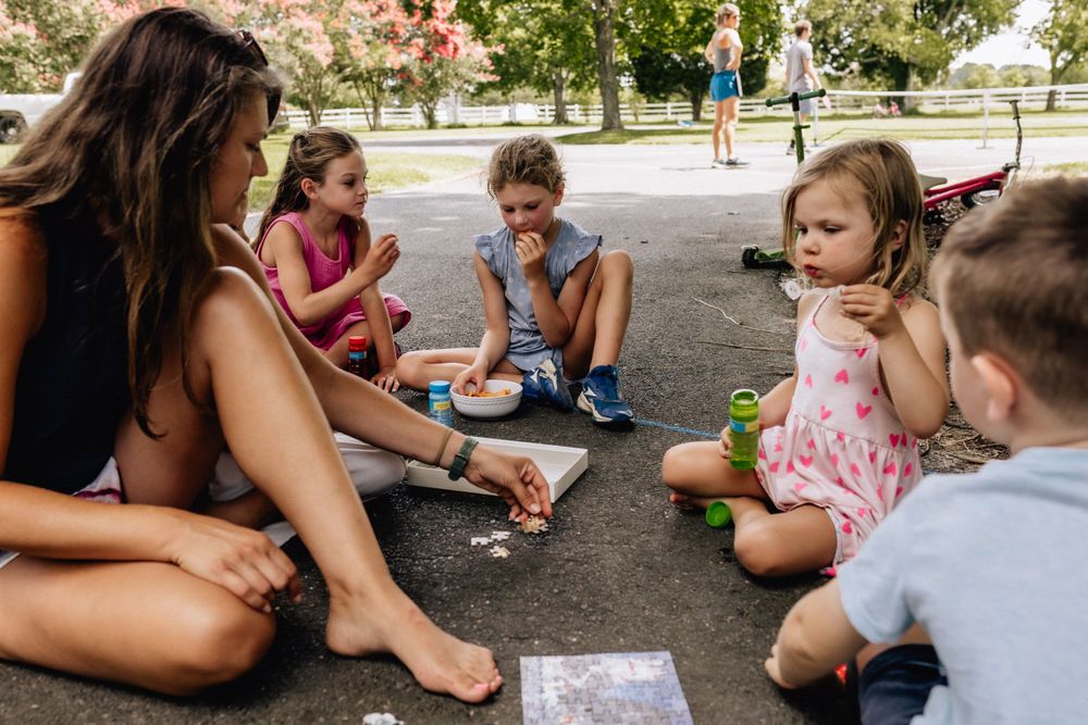 mother sitting on the driveway with children blowing bubbles and drawing with chalk