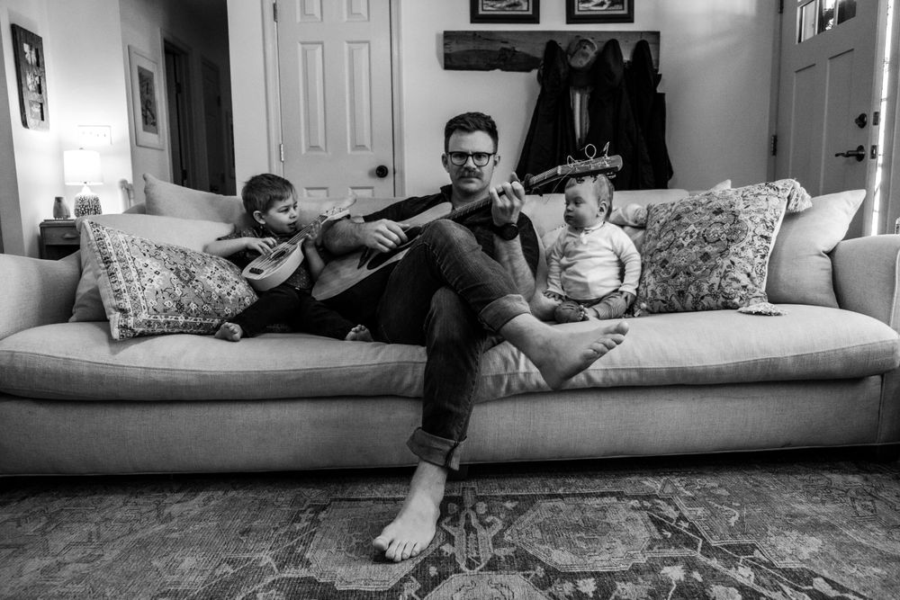 black and white portrait dad playing guitar on the couch with 2 toddlers in their chesapeake home