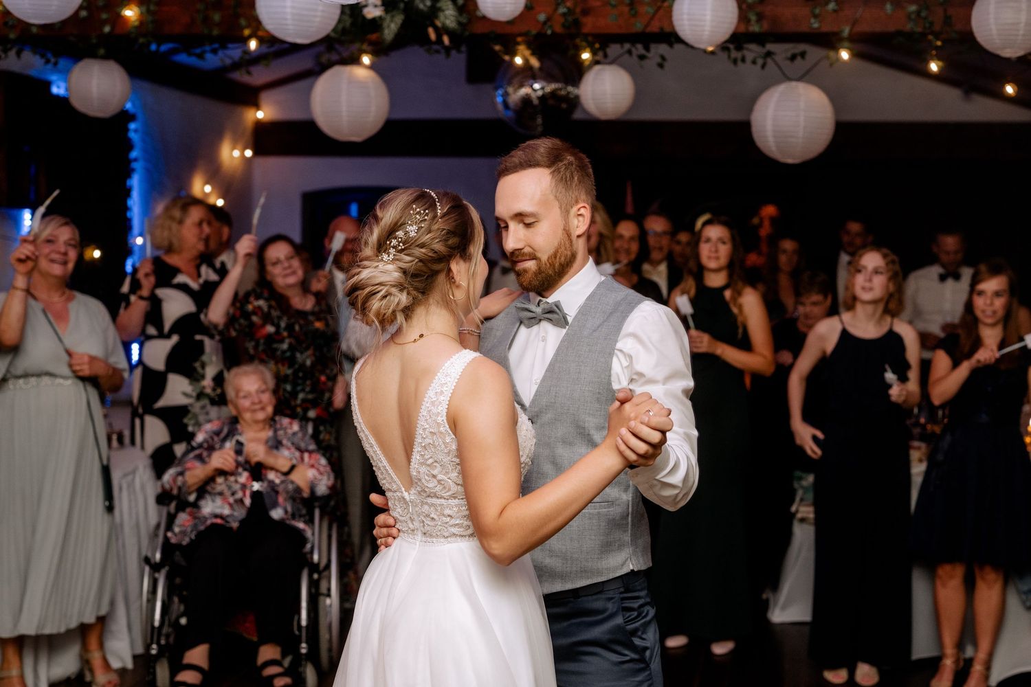 A couple sharing their first dance at a wedding reception under hanging paper lanterns.