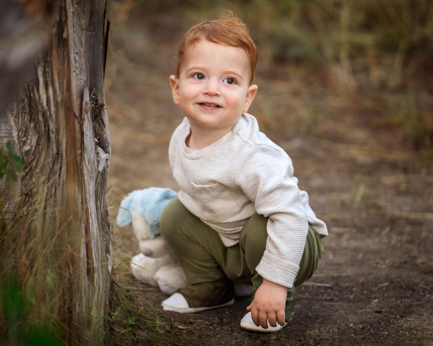 toddler boy squatting down holding a blue and white toy dog at Phil Hardberger Park