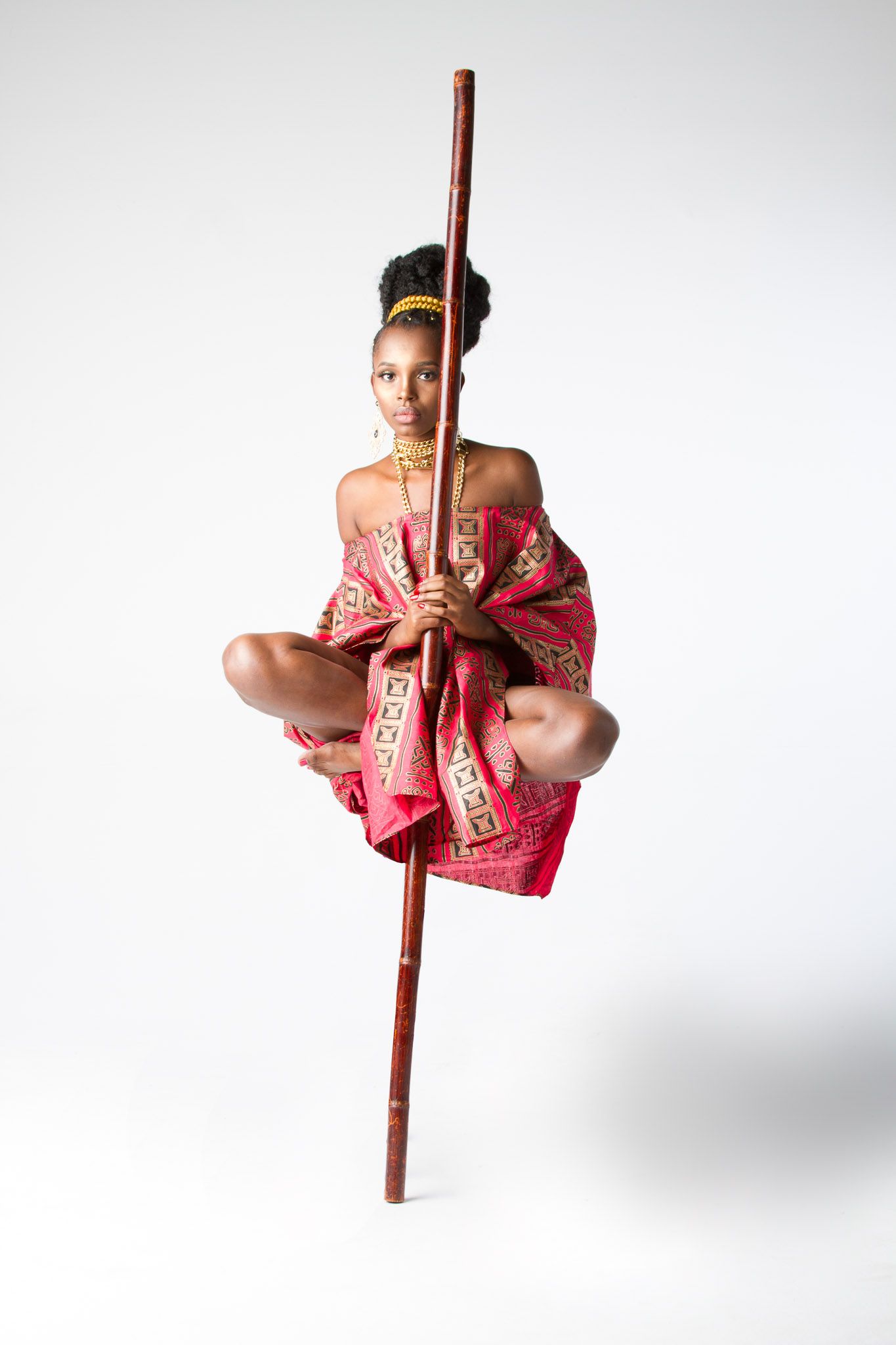 Young performer in red costume balances on wooden pole against white background.