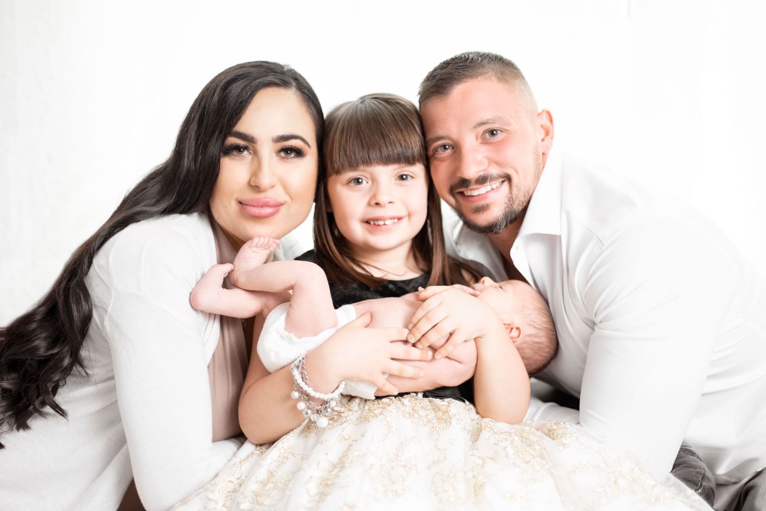 Family portrait session with parents and child wearing coordinated white outfits against a bright background.