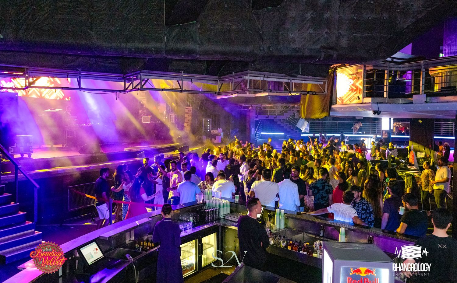 Nightclub or event space filled with guests under dramatic blue and purple lighting effects.