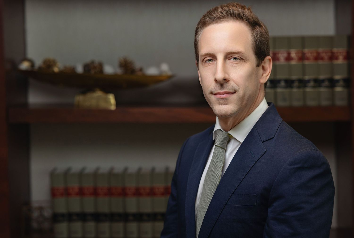 Professional male attorney in navy suit posing in front of law library.