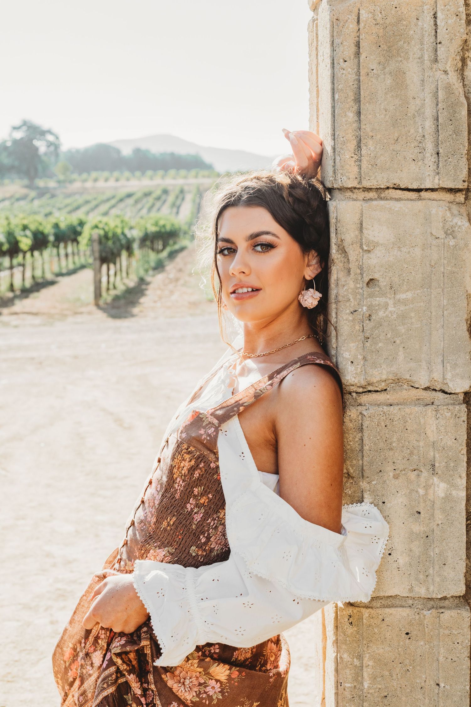 Editorial style portraits against rustic stone pillars with vineyard backdrop.