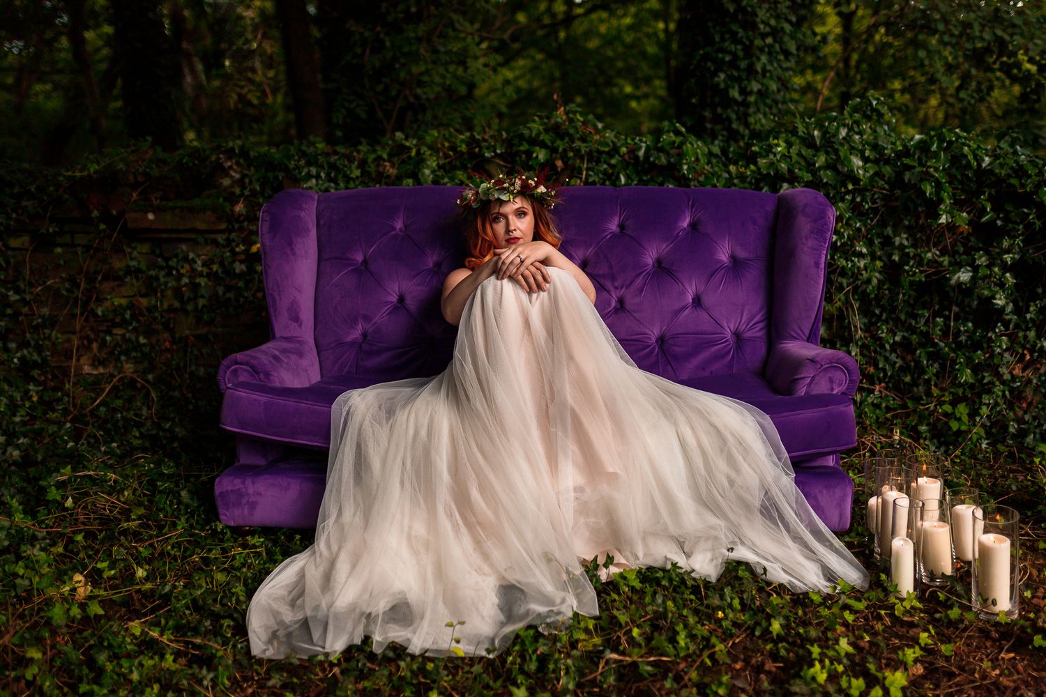 Ethereal bridal portrait on purple velvet couch outdoors with candles and flowy dress.