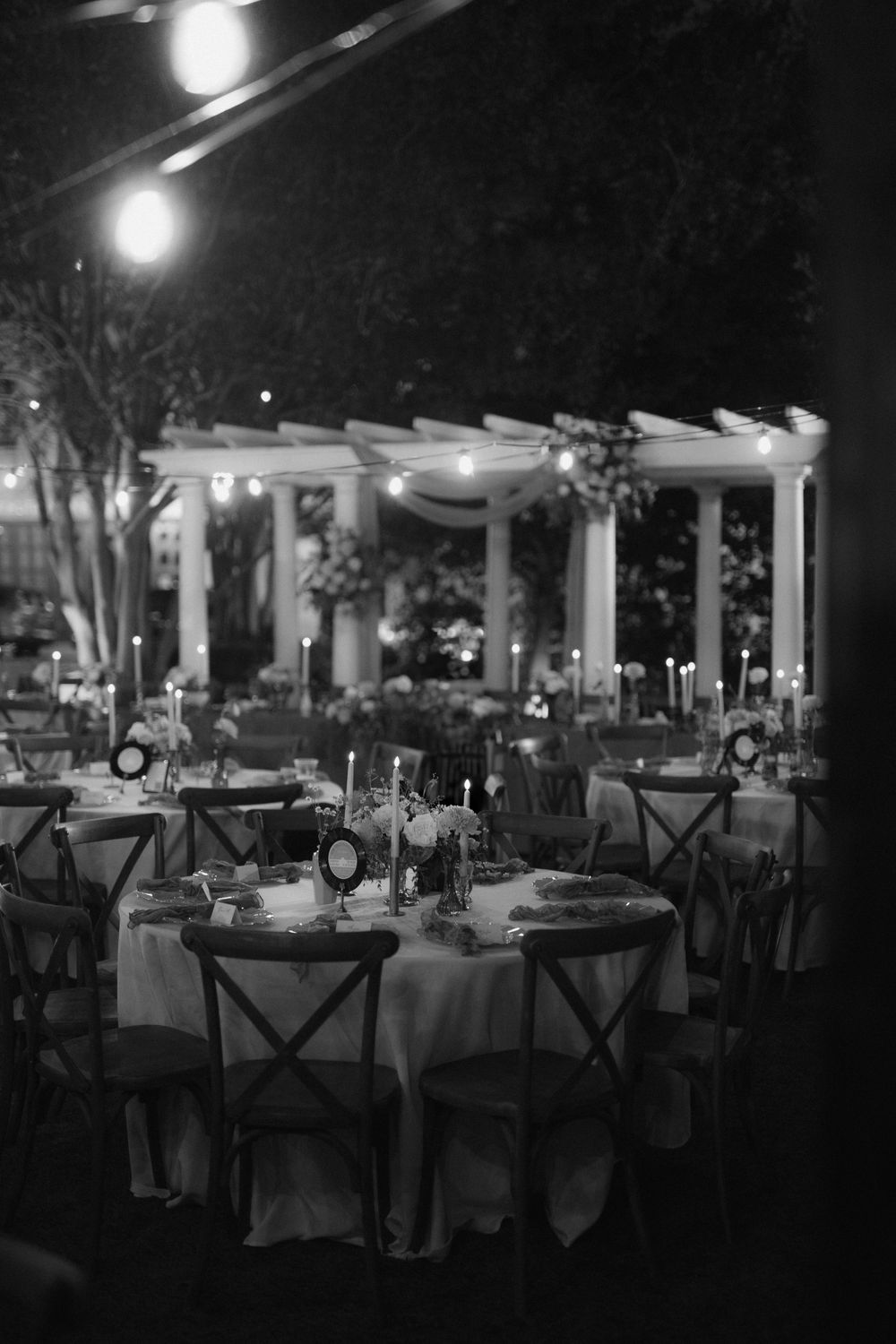 Elegant reception tables set with white linens and centerpieces under romantic outdoor lighting at night.