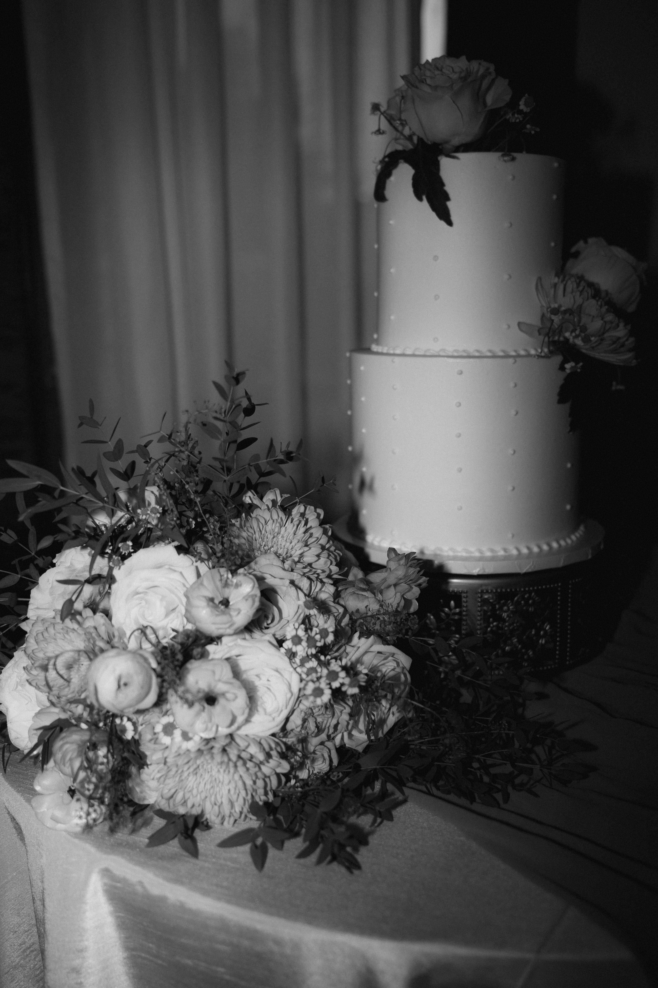 White floral arrangements with roses adorn a wedding cake table in dramatic lighting.