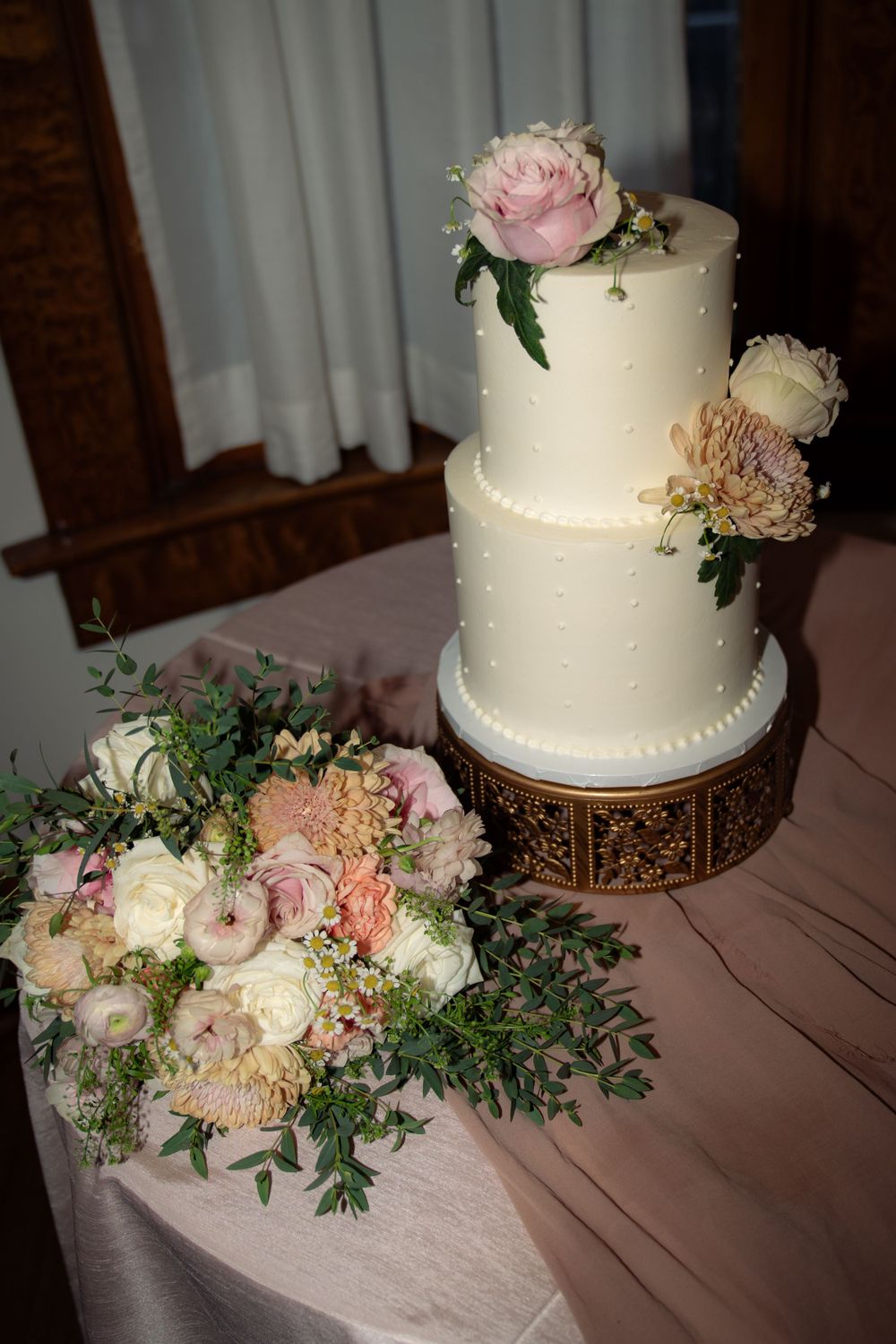 Elegant white wedding cake decorated with fresh pink roses and greenery on a wooden stand.