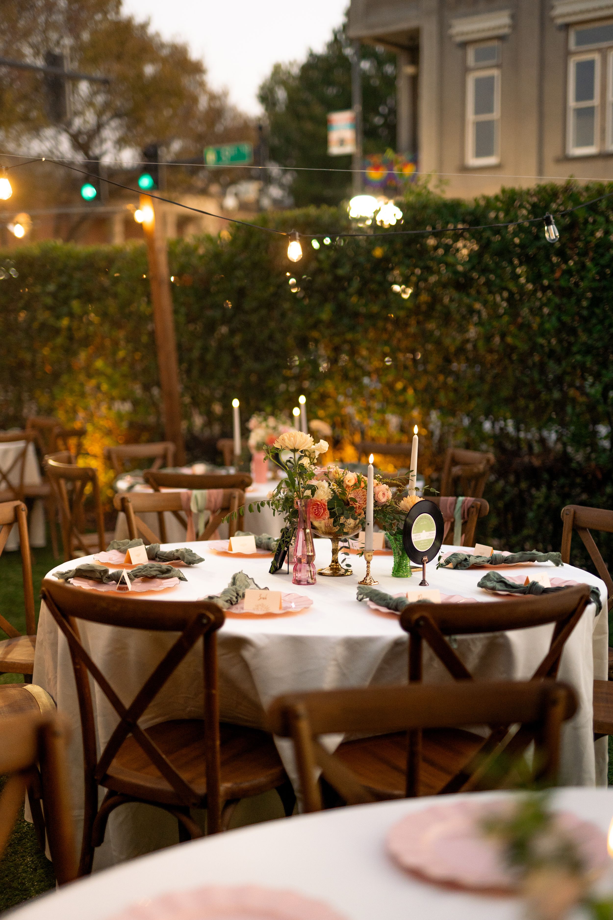 Outdoor wedding reception tables with vintage-inspired decor and cross-back chairs at dusk.