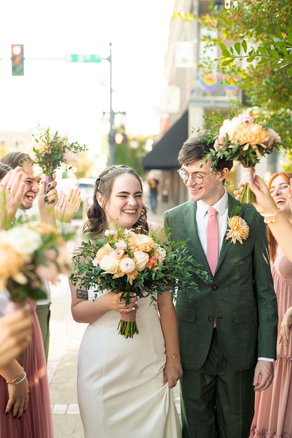 Wedding party celebrating outdoors with peach and blush floral bouquets in natural sunlight.
