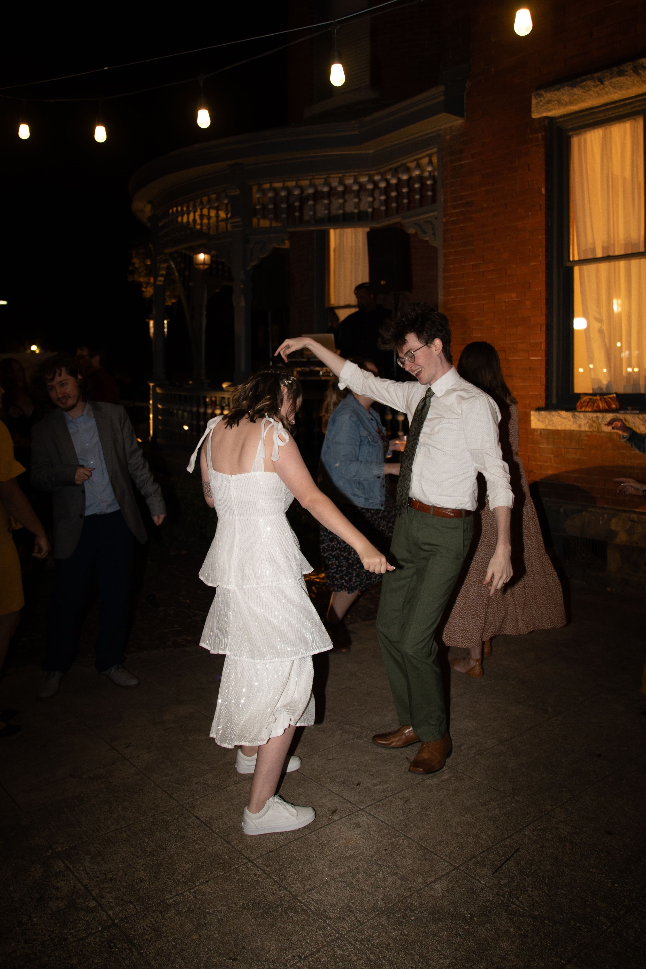 Dancing guests celebrate at an outdoor evening reception under string lights.