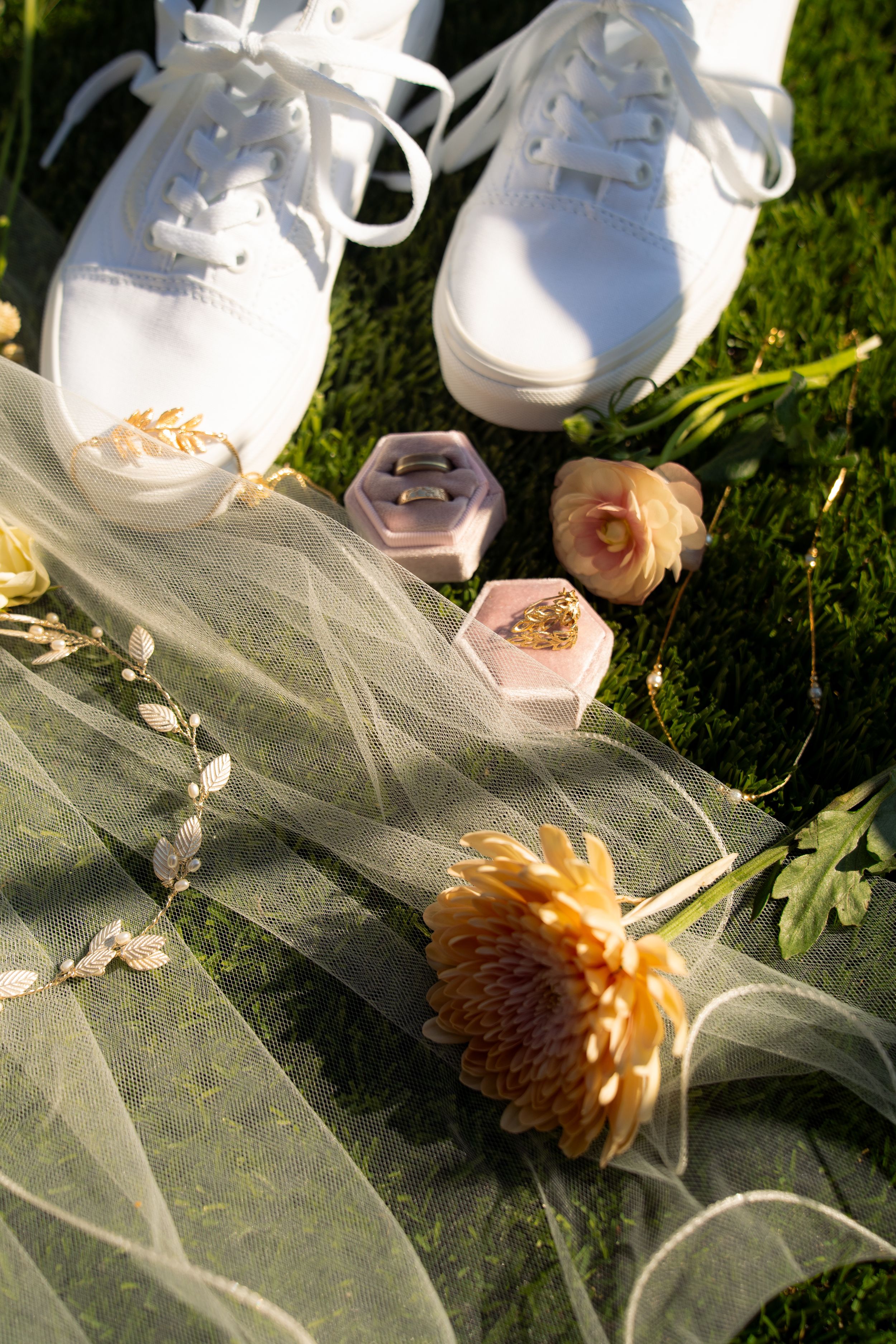 Wedding accessories and delicate flowers arranged on tulle fabric in natural sunlight.