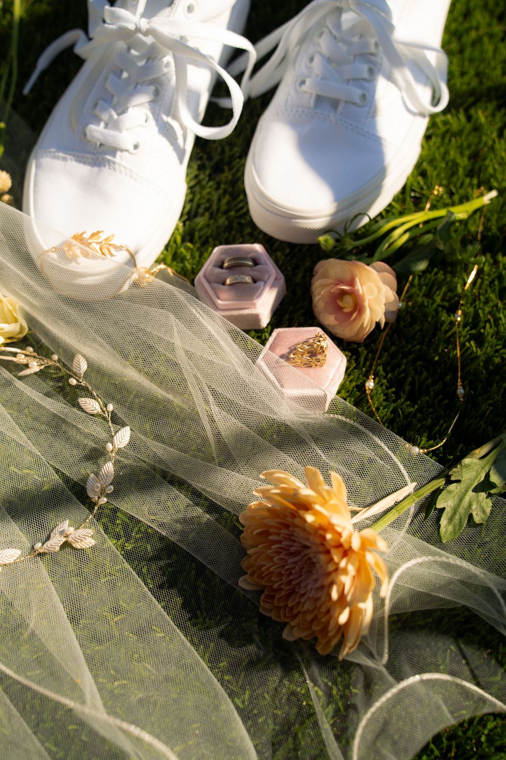 Wedding accessories and delicate flowers arranged on tulle fabric in natural sunlight.