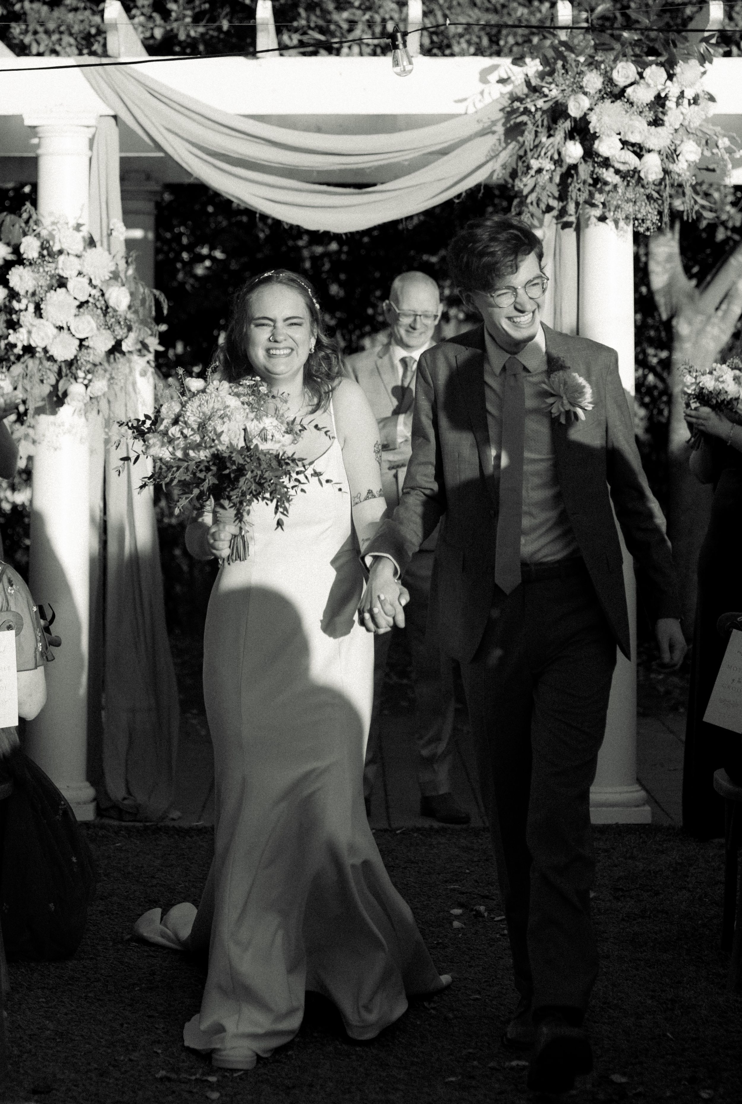 Black and white wedding photo under decorated pergola with floral arrangements.