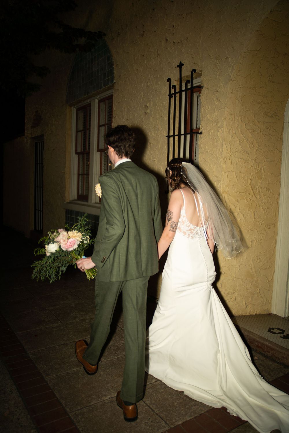Wedding couple walking along a dimly lit vintage building exterior.