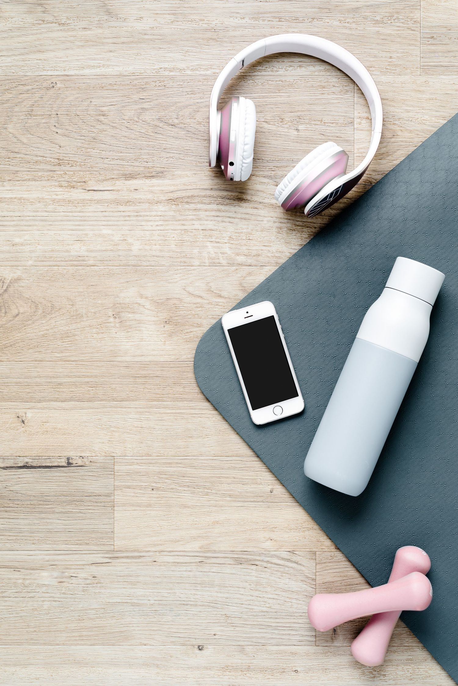 Pale blue water bottle, pink headphones, iPhone and pink weights on top of a blue yoga mat. Fitness, health, exercise