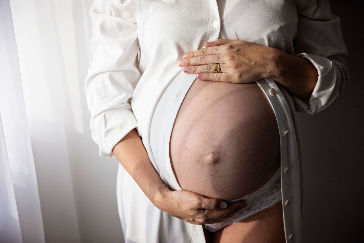 A close-up photograph shows hands cradling a pregnant belly in white clothing against a light background.