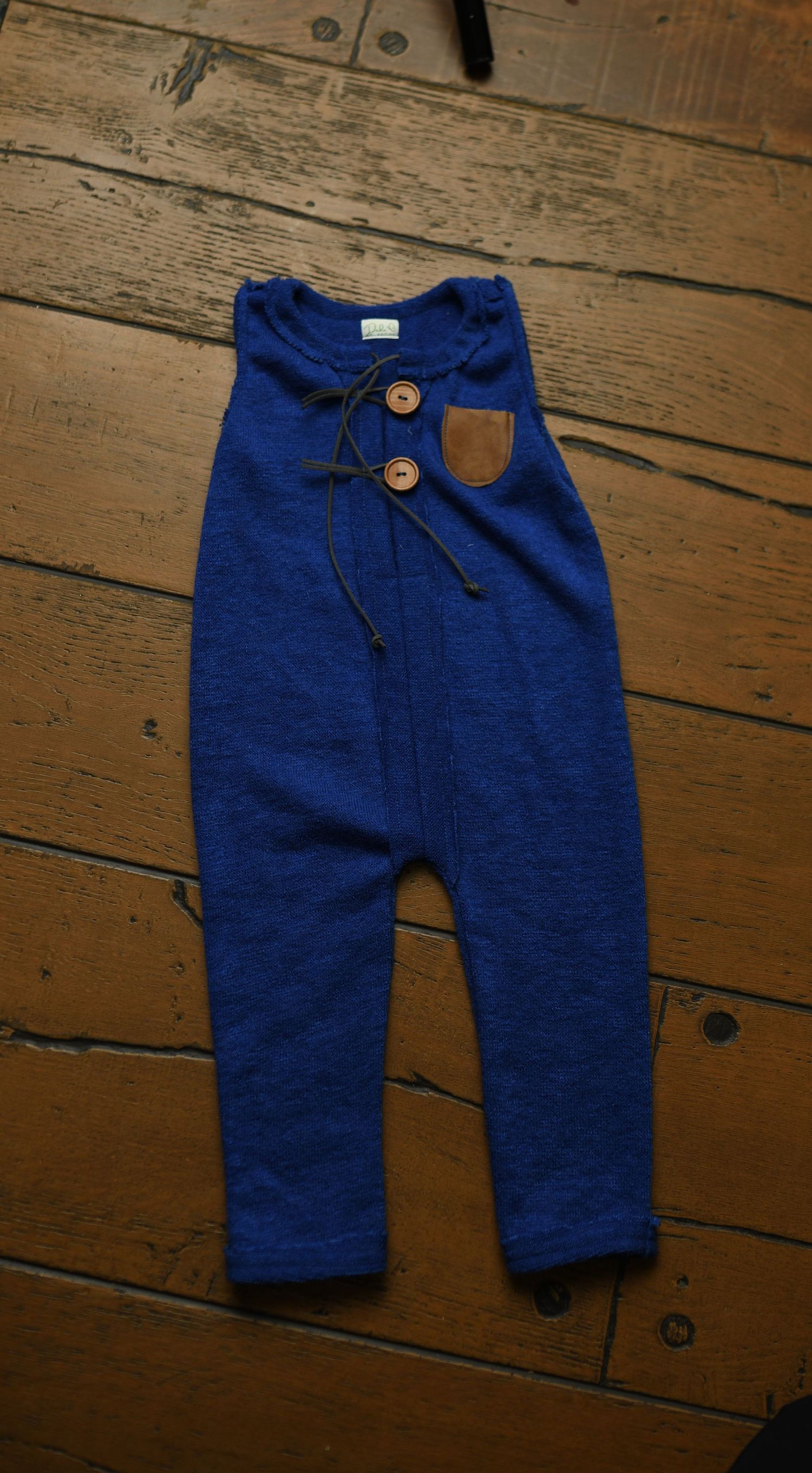 Navy blue baby pants with brown leather accent displayed on wooden floor.