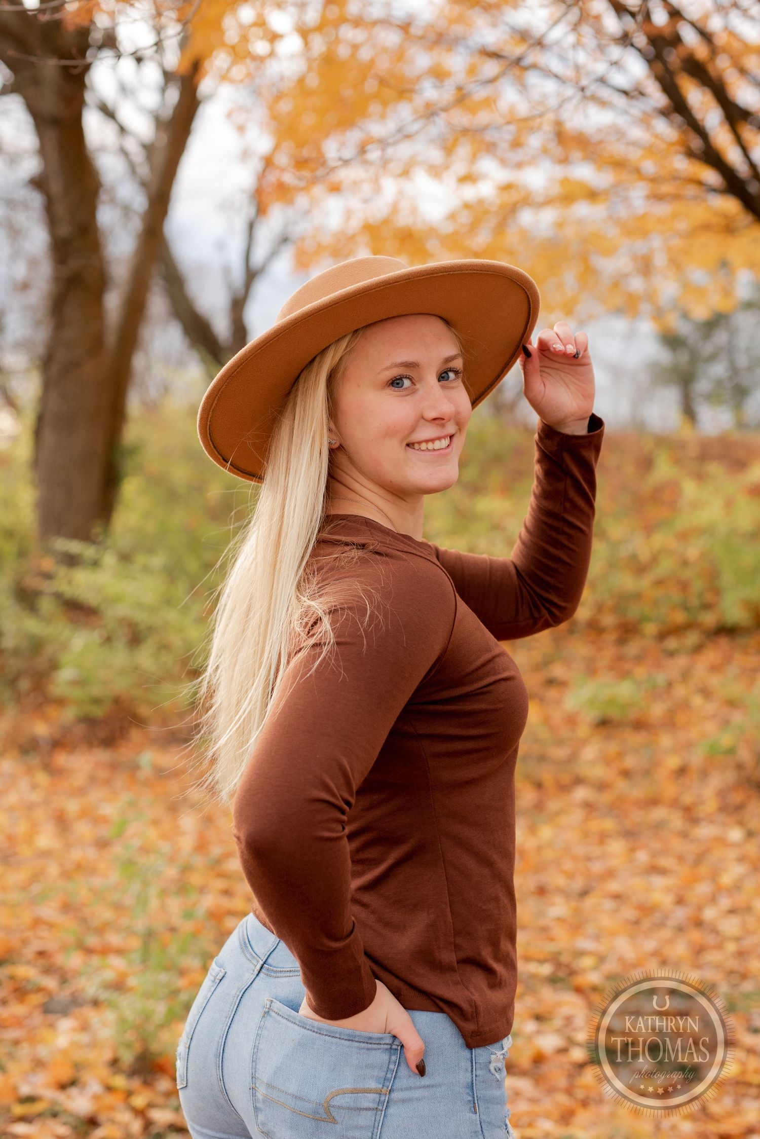 Outdoor autumn portrait with brown sweater and tan hat against a background of fall foliage.