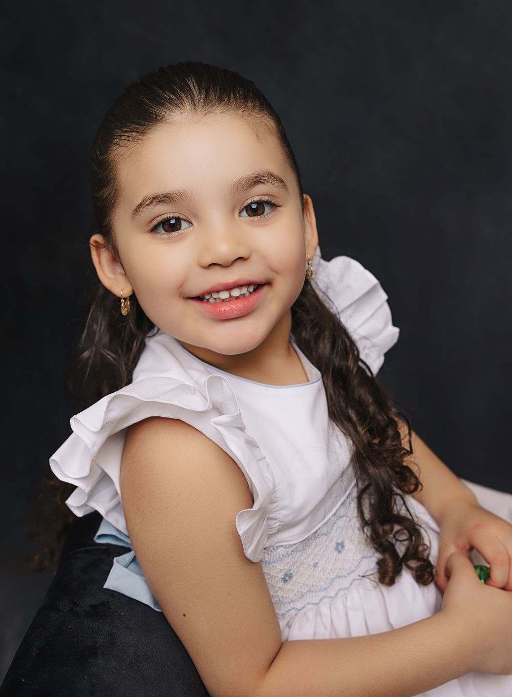 A portrait of someone in a white ruffled dress with long curly hair against a dark background.