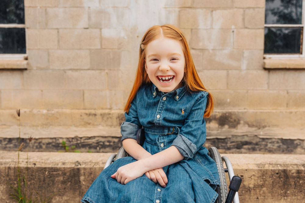 Young person in denim dress sits smiling on stone steps.