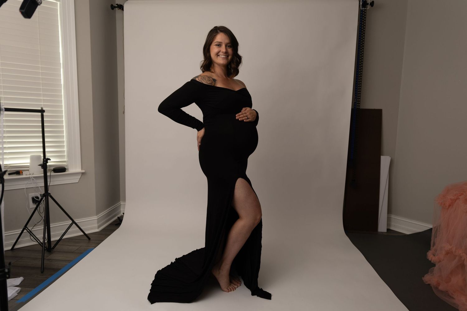 Maternity photo of woman in black formal dress against white backdrop.