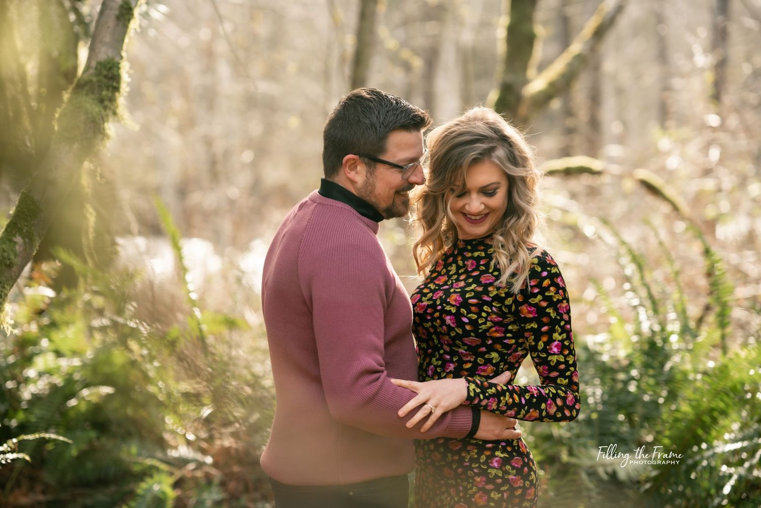 Expecting couple sharing tender moment in sunlit forest setting.