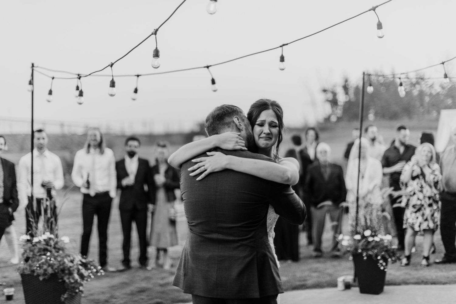 Couple dancing at an outdoor event under string lights at dusk.