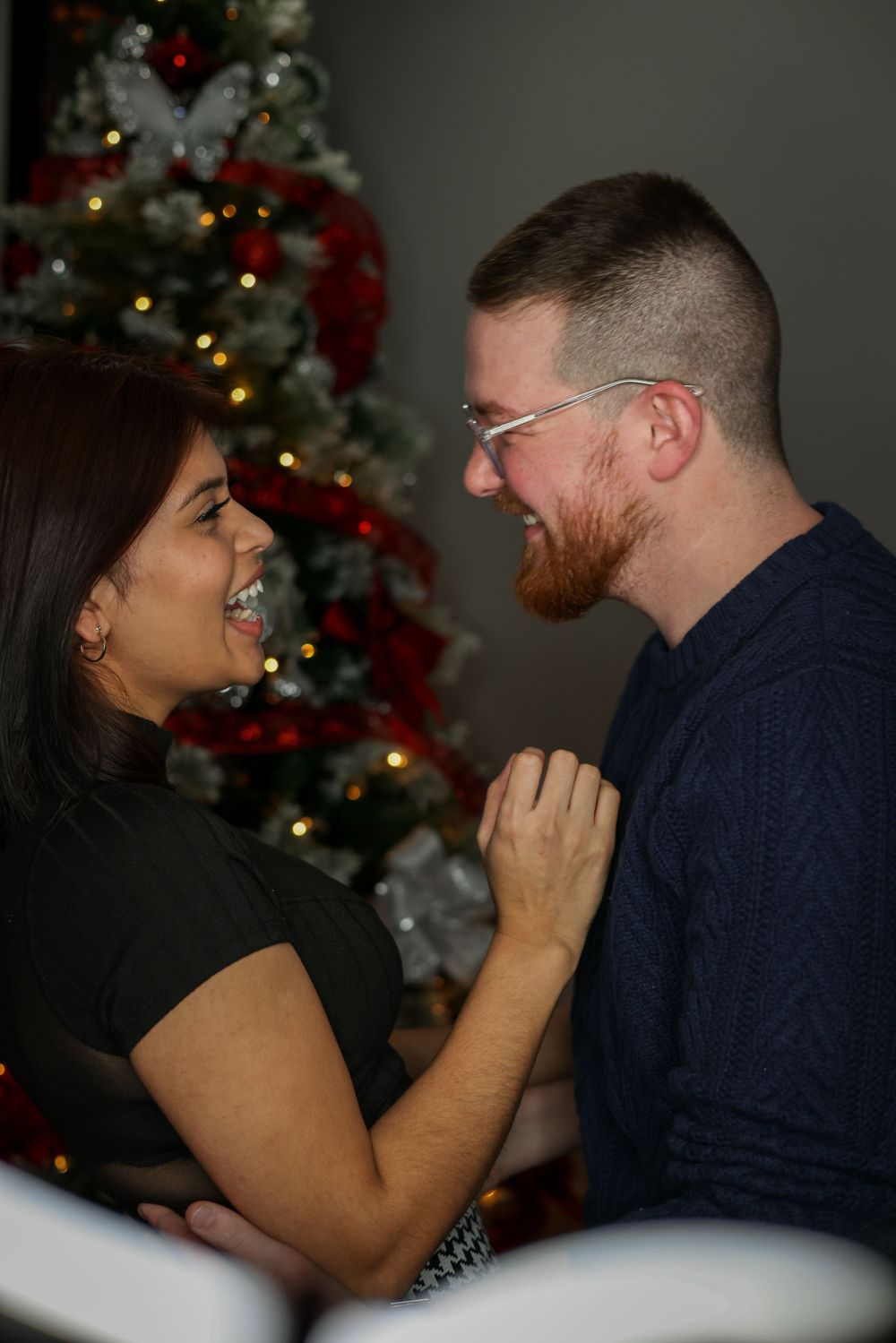 A couple shares genuine laughter during their holiday photo session by the Christmas tree.