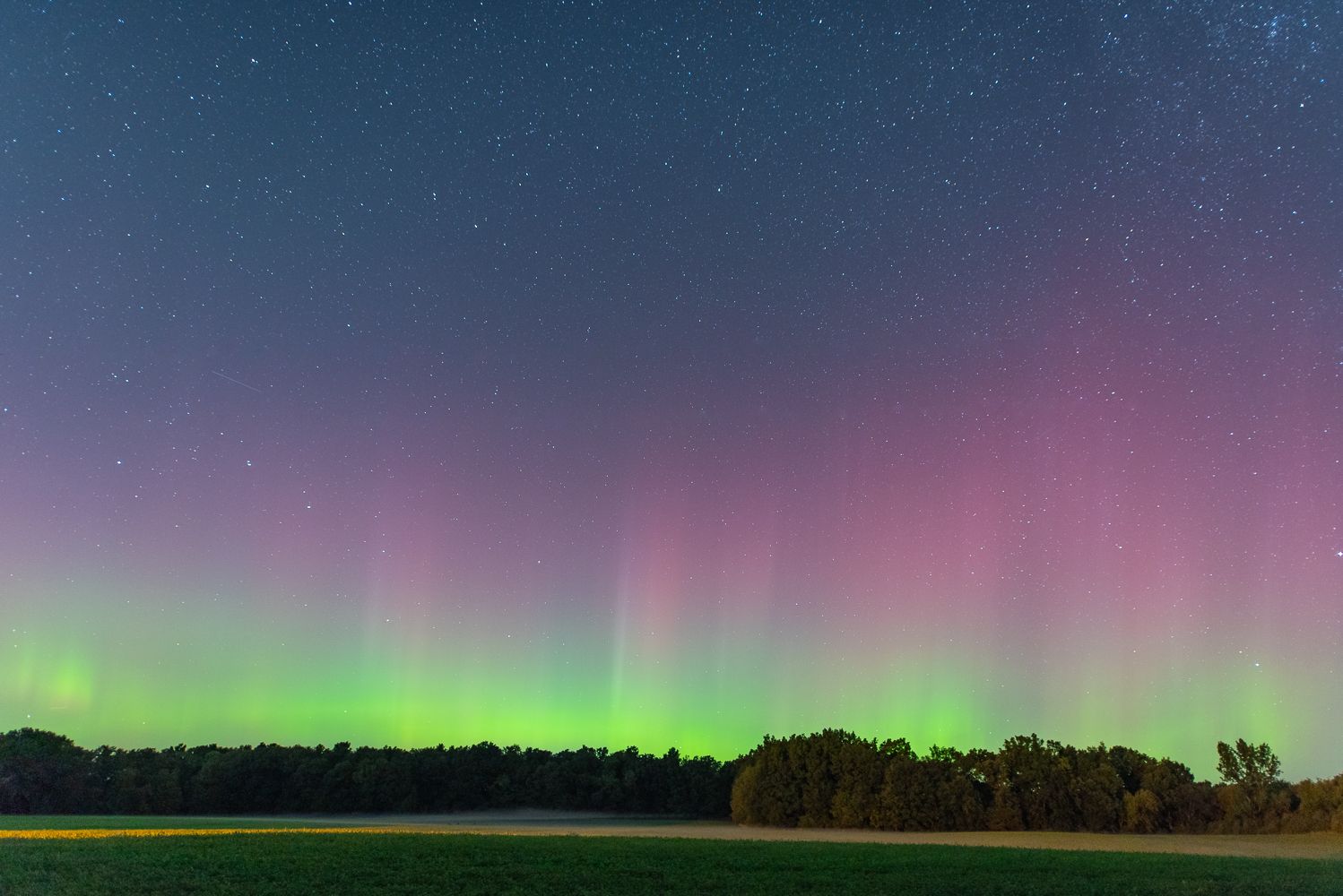 Stunning aurora borealis display illuminates the night sky with pink and green lights over a dark landscape.