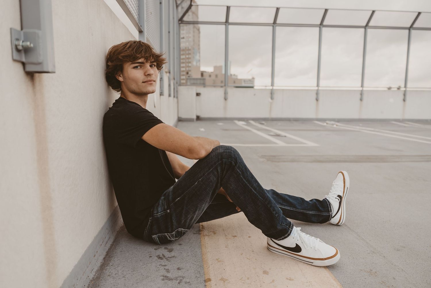 Person sitting casually on steps of urban building wearing dark pants and white sneakers.