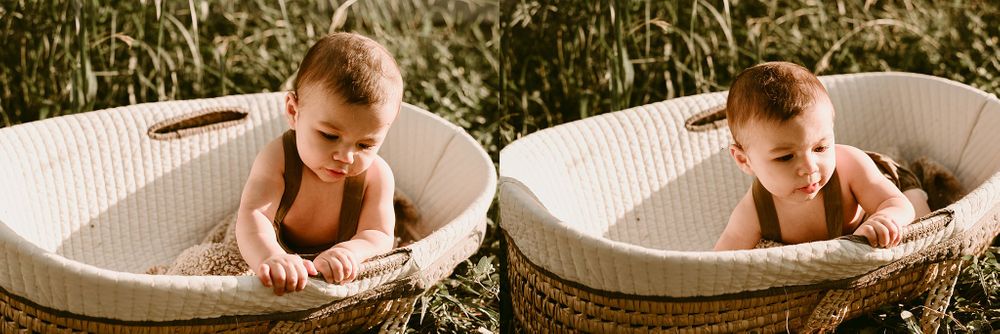 Baby wearing brown overalls explores white woven bassinet outdoors in sunlight.