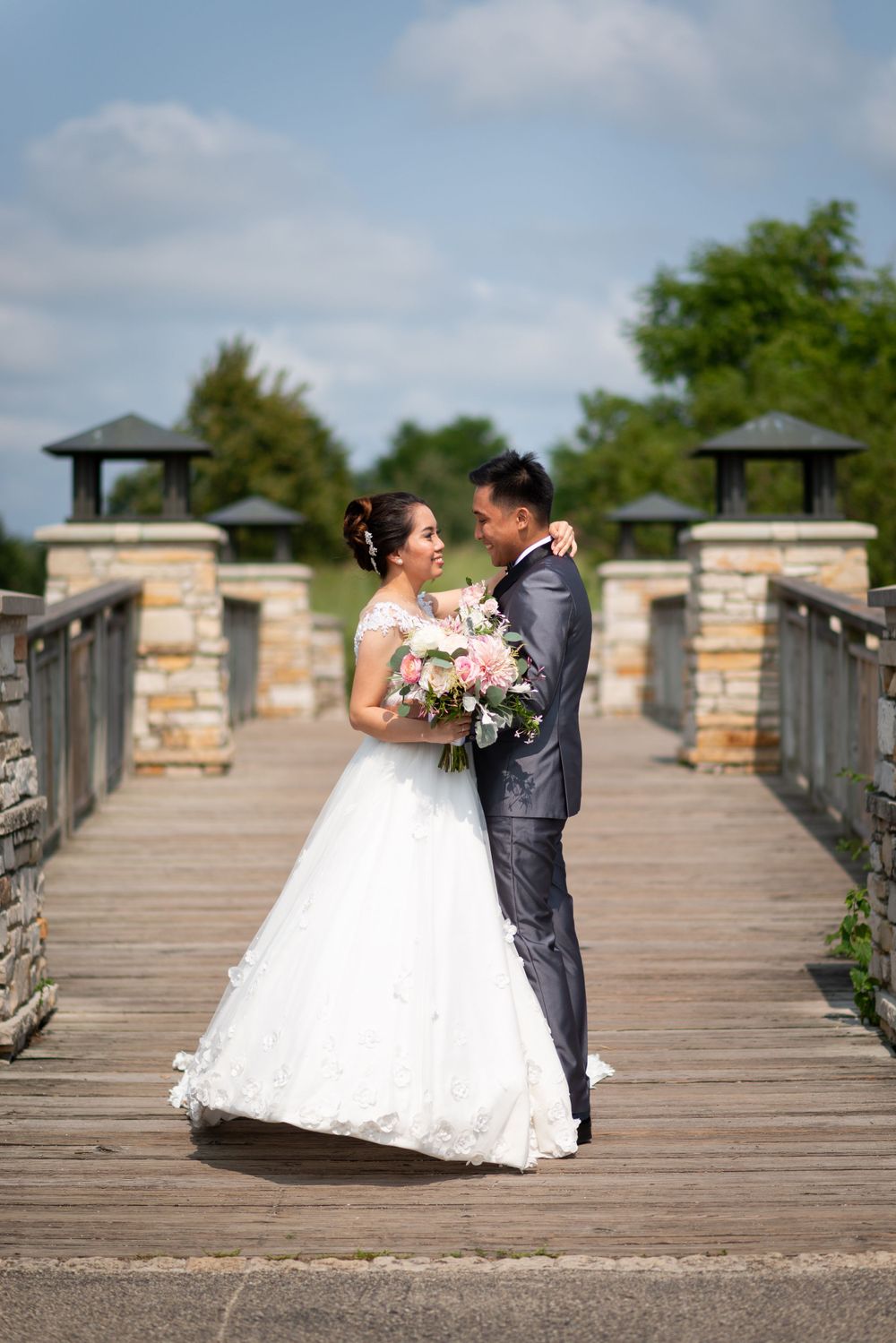 Wedding couple shares romantic moments on a stone-pillared wooden bridge.