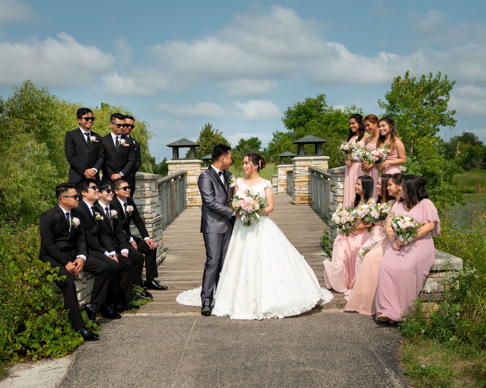 Wedding party poses on a rustic bridge with bridesmaids in pink and groomsmen in black suits.