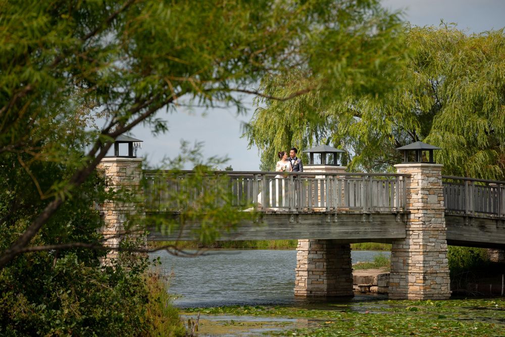 A scenic stone bridge with decorative pillars spans across water surrounded by willow trees.