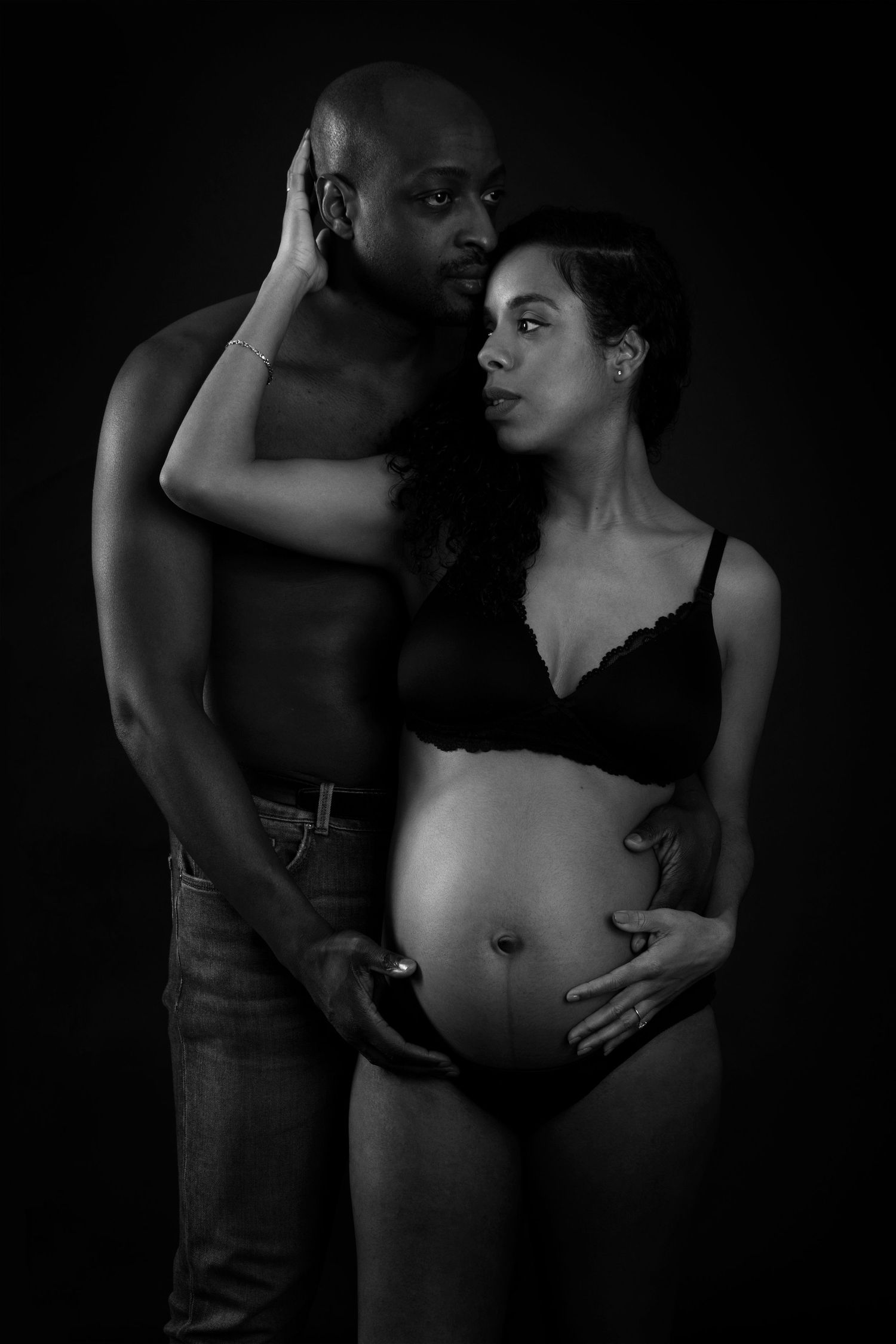 An intimate black and white maternity portrait against a dark background.
