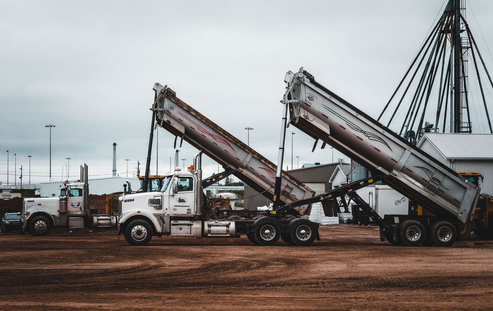 Row of dump trucks with raised beds lined up at a construction site.