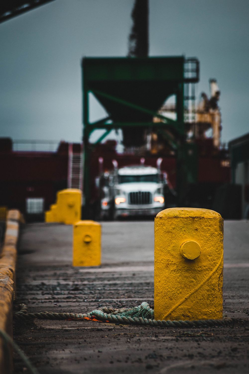 Yellow safety bollards lined up on concrete surface at industrial worksite.