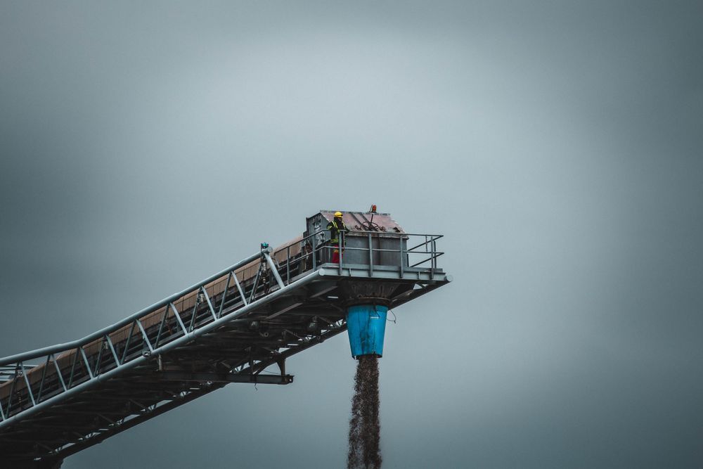 Industrial conveyor belt system against moody gray sky at construction site.