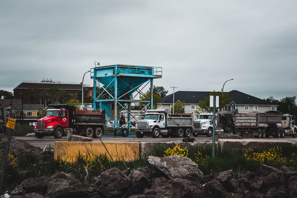 Industrial site with dump trucks and equipment visible against an overcast sky.