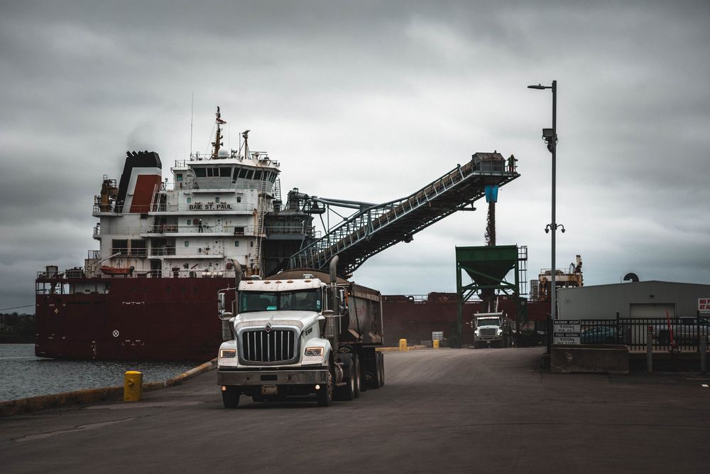 Industrial port facility with trucks and loading equipment under overcast sky.