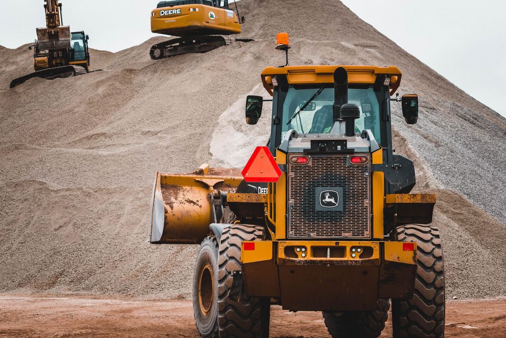 Yellow construction vehicles and equipment lined up at a work site during daytime.