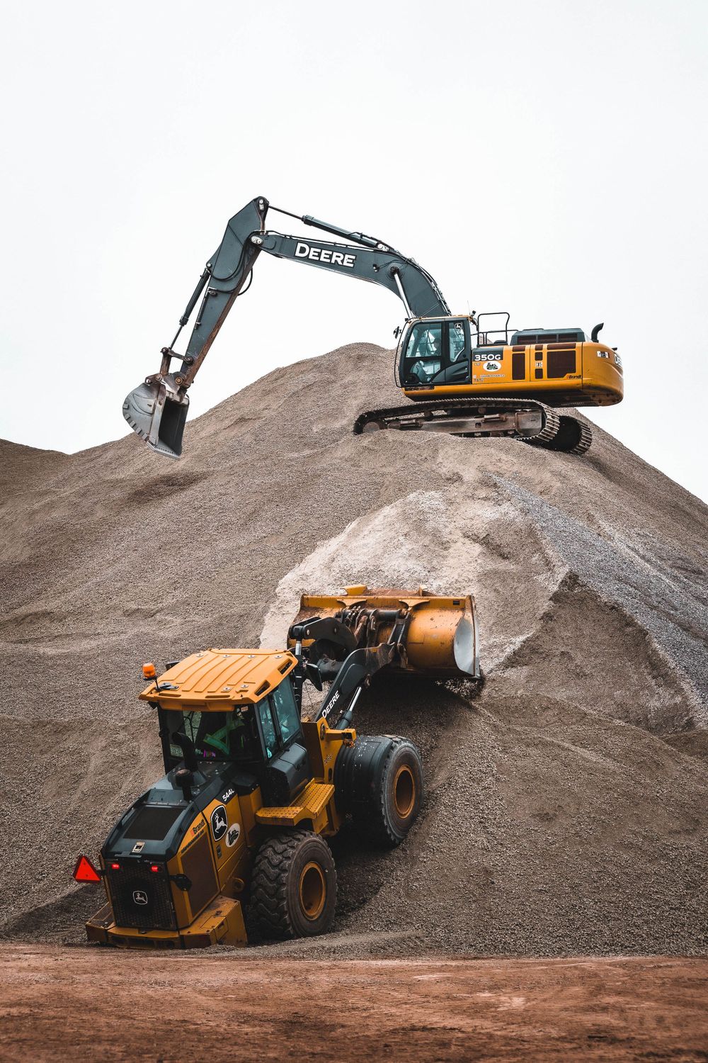 Yellow excavator and construction vehicles working on large dirt piles.