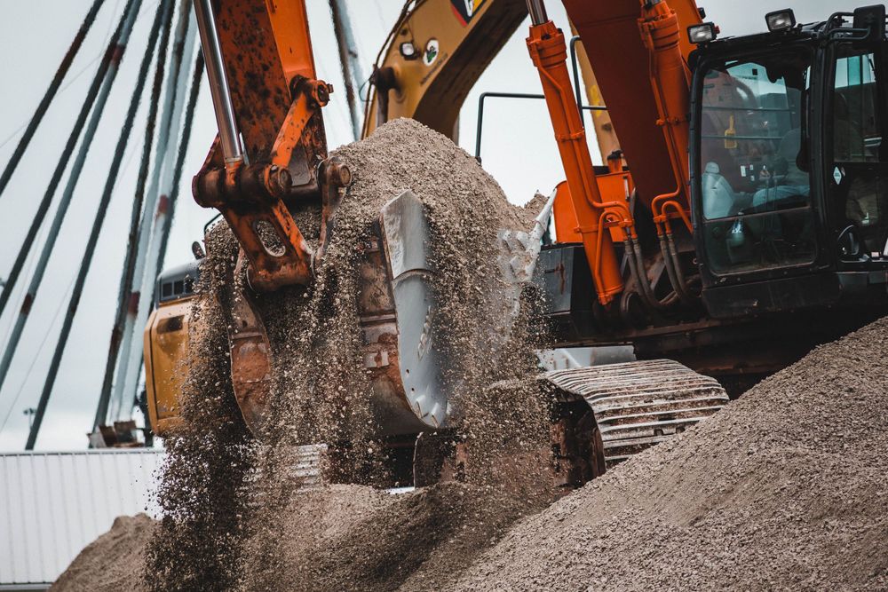 Orange excavator machinery working with gravel and dirt piles at an industrial construction site.