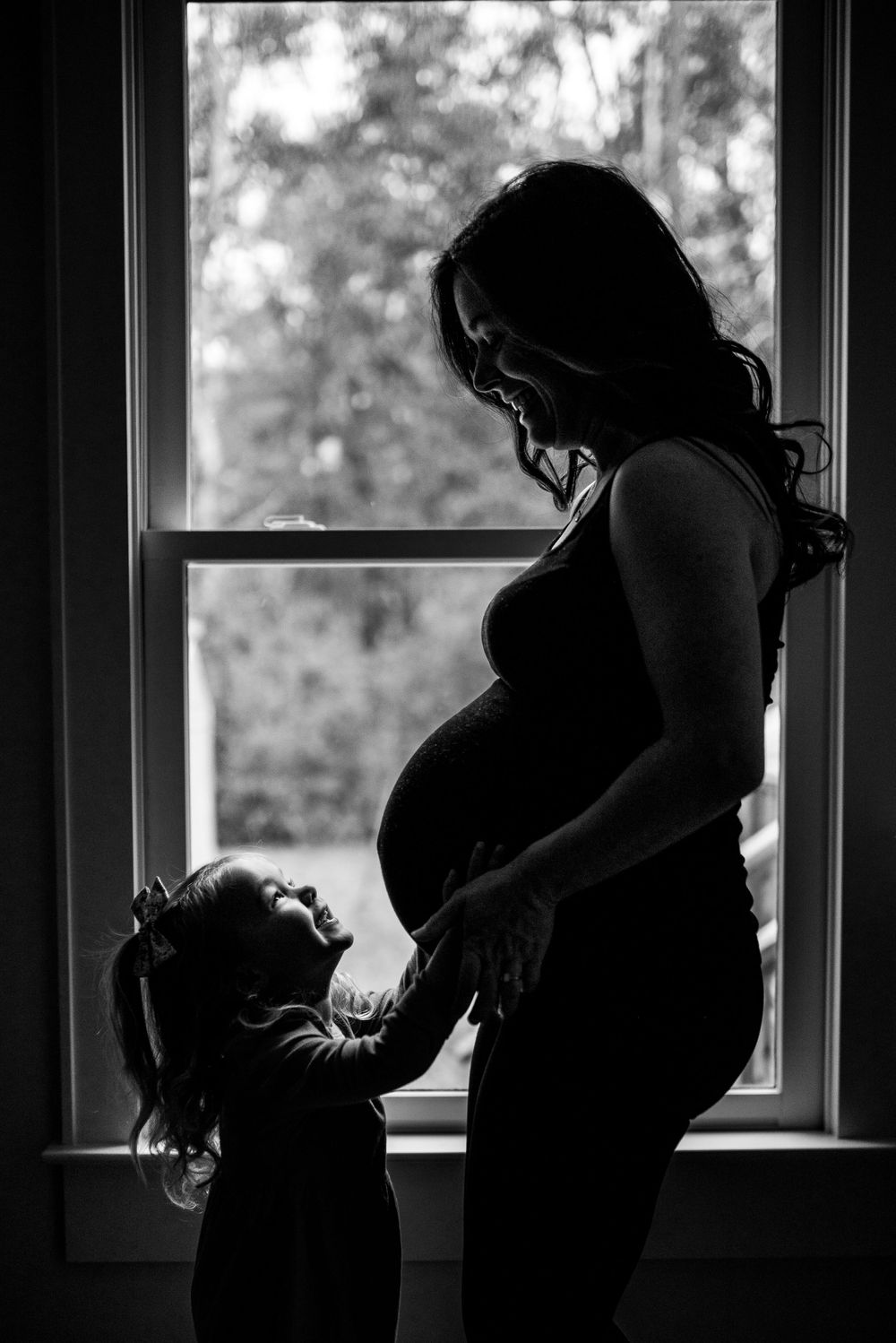 A silhouette of two figures standing by a window in an intimate family moment.