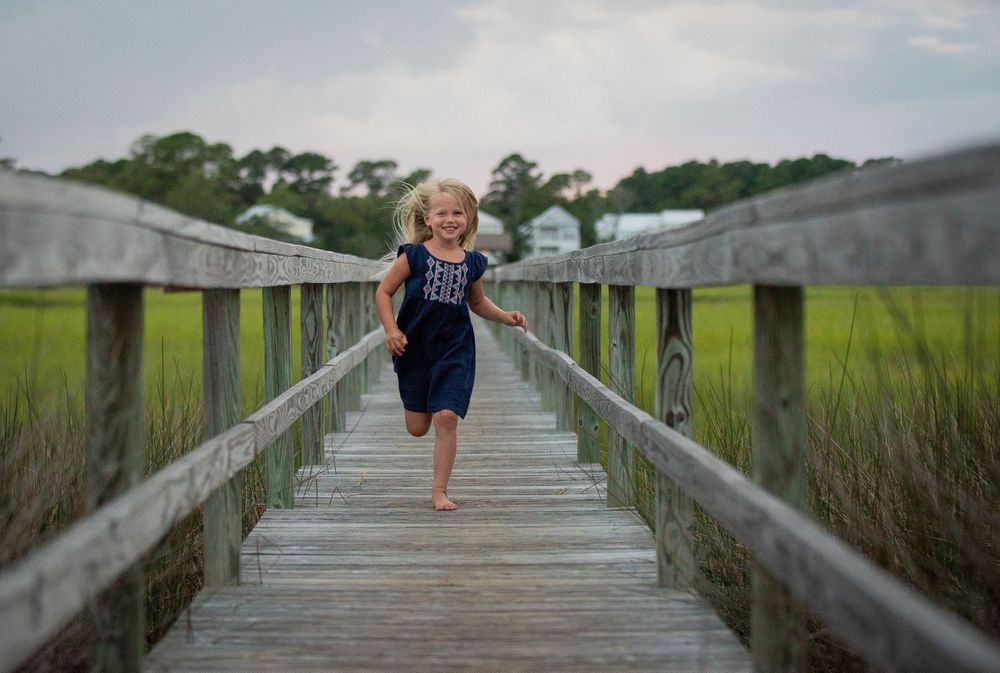 A joyful child runs along a wooden boardwalk over coastal marshland.